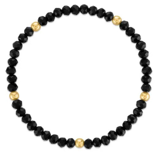 A beaded stretch bracelet featuring faceted black beads and four polished gold spacer beads, displayed on a clean white background.