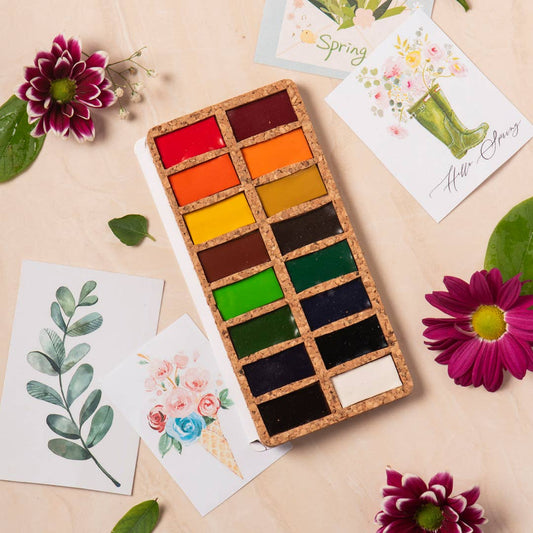 Set of watercolor paints with a spring-themed card and flowers on a light background