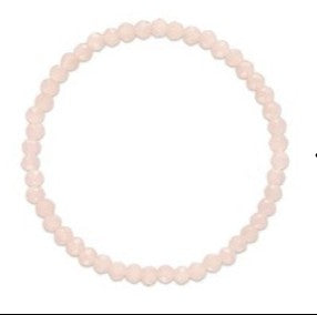 A pale pink beaded stretch bracelet arranged in a circle on a plain white background.