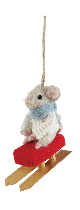 A small felted wool mouse ornament wearing a white sweater and blue scarf, sitting on a red sled with wooden runners and hanging from a natural jute rope against a white background.