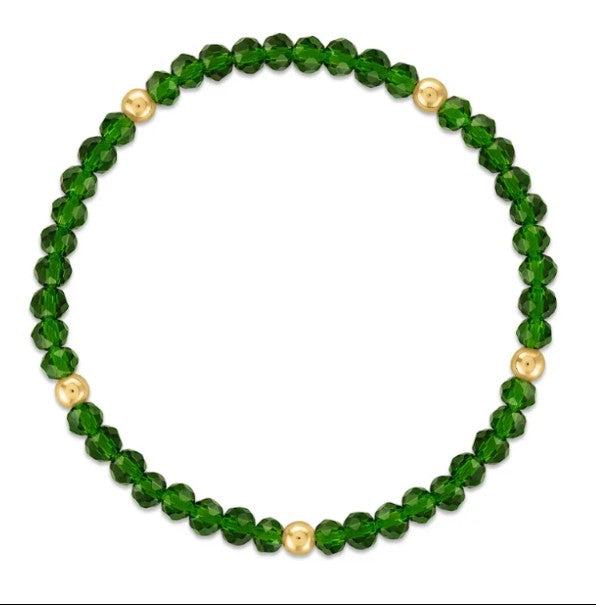 A beaded stretch bracelet featuring faceted green beads and five small polished gold spacer beads, displayed on a clean white background.