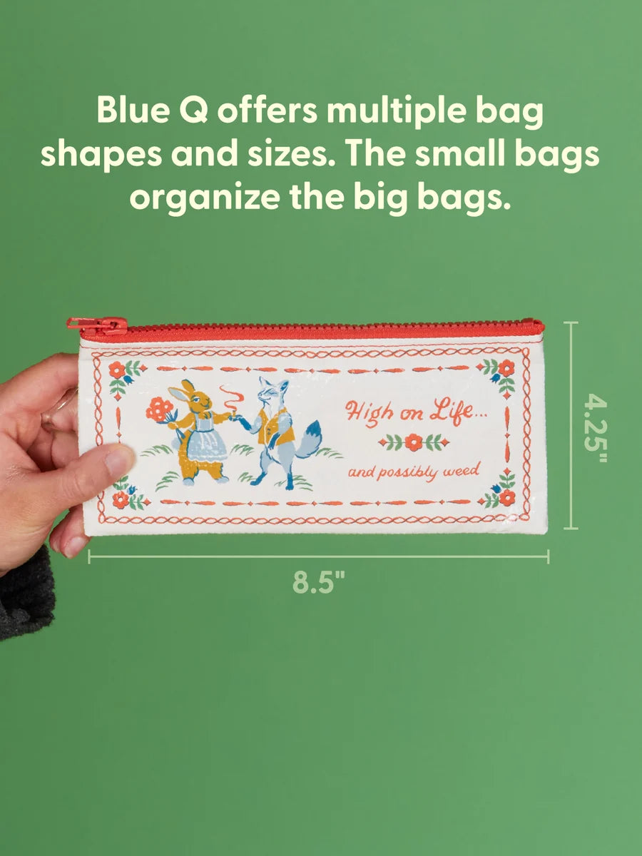 A hand holds a small illustrated zip pouch against a green background with text explaining Blue Q bag organization. The pouch is cream with red trim and a whimsical bunny-and-fox design, with dimension labels showing 8.