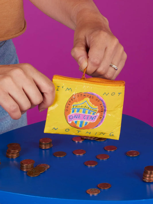 Person counting coins with a colorful 'I'm Not Nothing' coin purse on a blue surface against a purple background