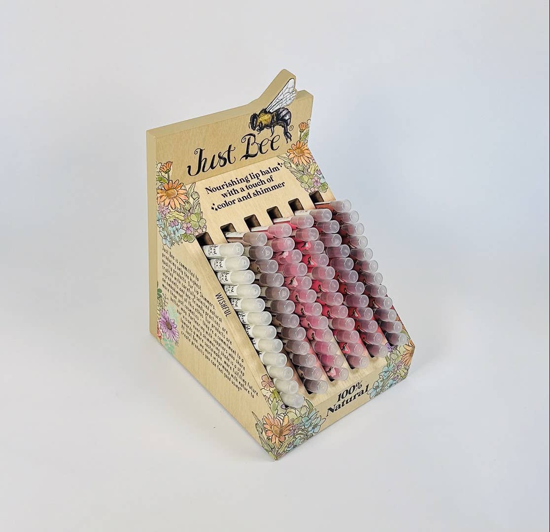 Display of Just Bee lip balm tubes with decorative packaging on a white background