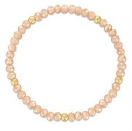 A beaded stretch bracelet featuring light peach-pink faceted beads separated by small gold spacer beads, shown on a plain white background.