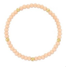A beaded stretch bracelet made of light peach-pink round beads with three small gold spacer beads, shown on a plain white background.