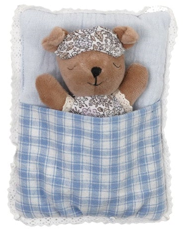 A plush teddy bear toy tucked inside a small pillow-shaped pouch with a blue-and-white plaid blanket and a light blue lining, wearing a matching floral sleep cap and white dress.