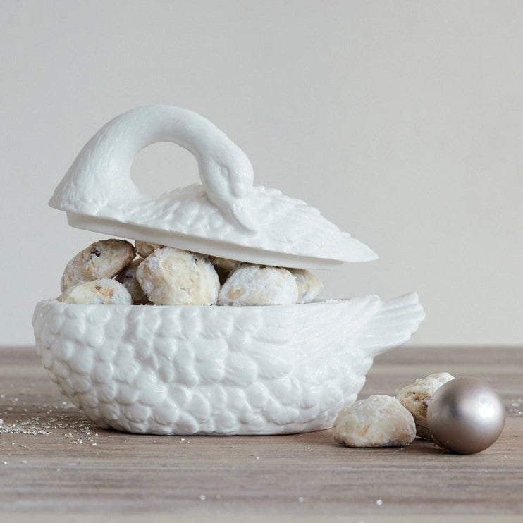 white swan-shaped ceramic bowl on a wooden surface with decorative items inside.
