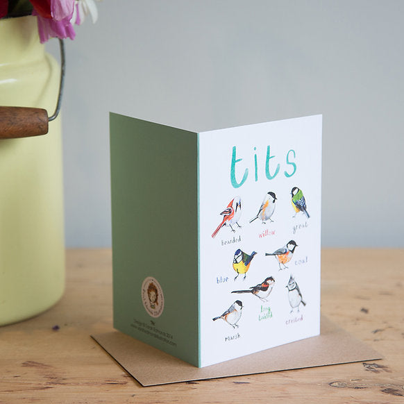 Card with illustrations of birds and text 'tits' on a wooden surface with a vase in the background.