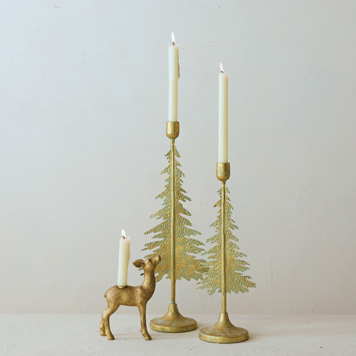 Decorative candle holders shaped like a deer, Christmas tree, and candle on a plain background