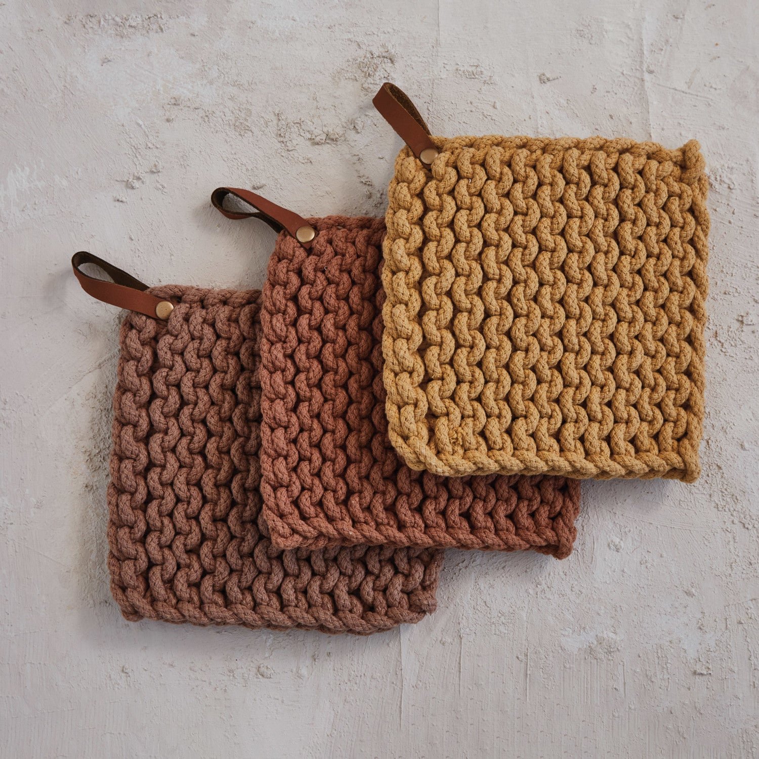 Cotton crocheted pot holders with leather straps on a textured surface.