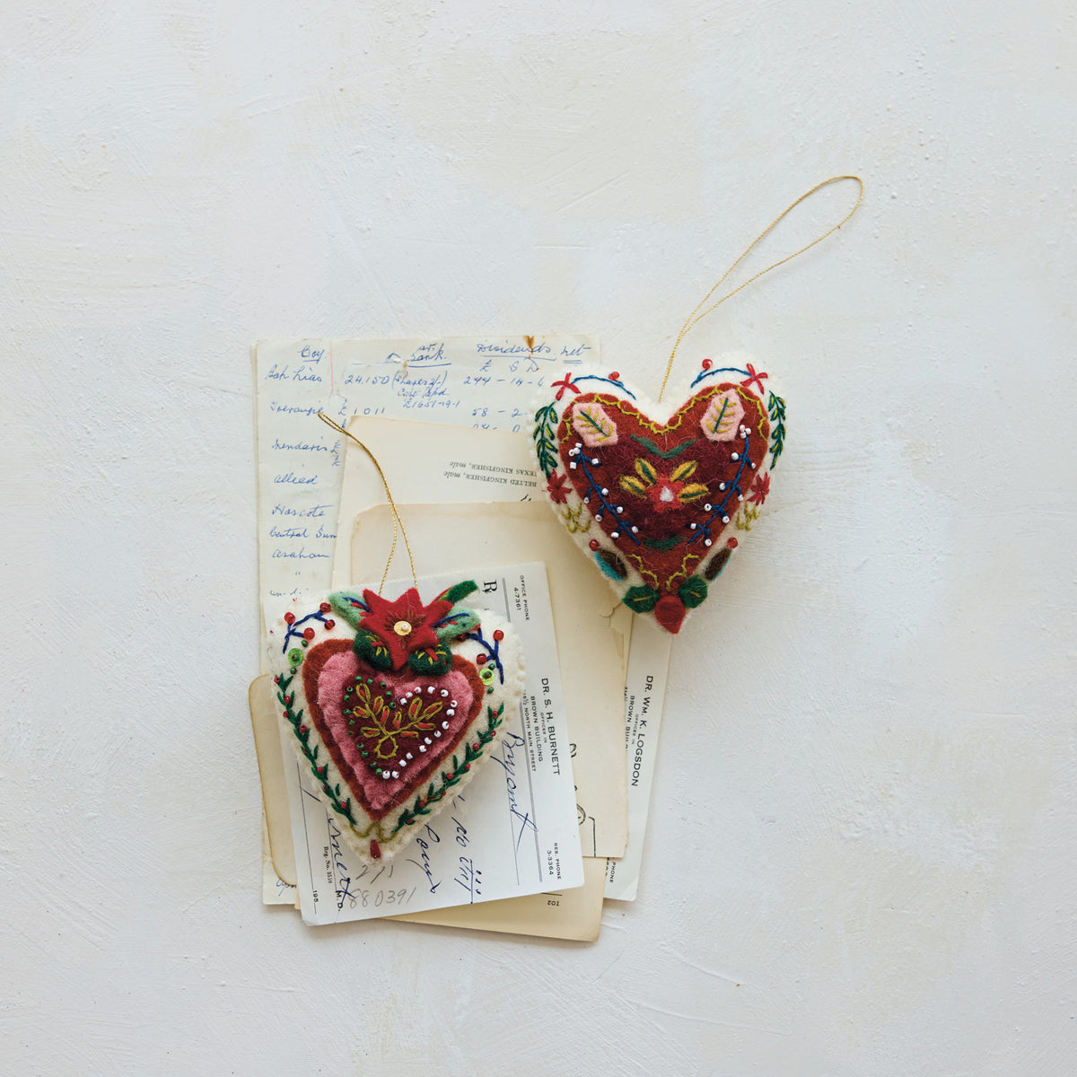 Two handmade wool felt heart ornaments styled with colorful embroidery, beaded embellishments, and hanging loops.