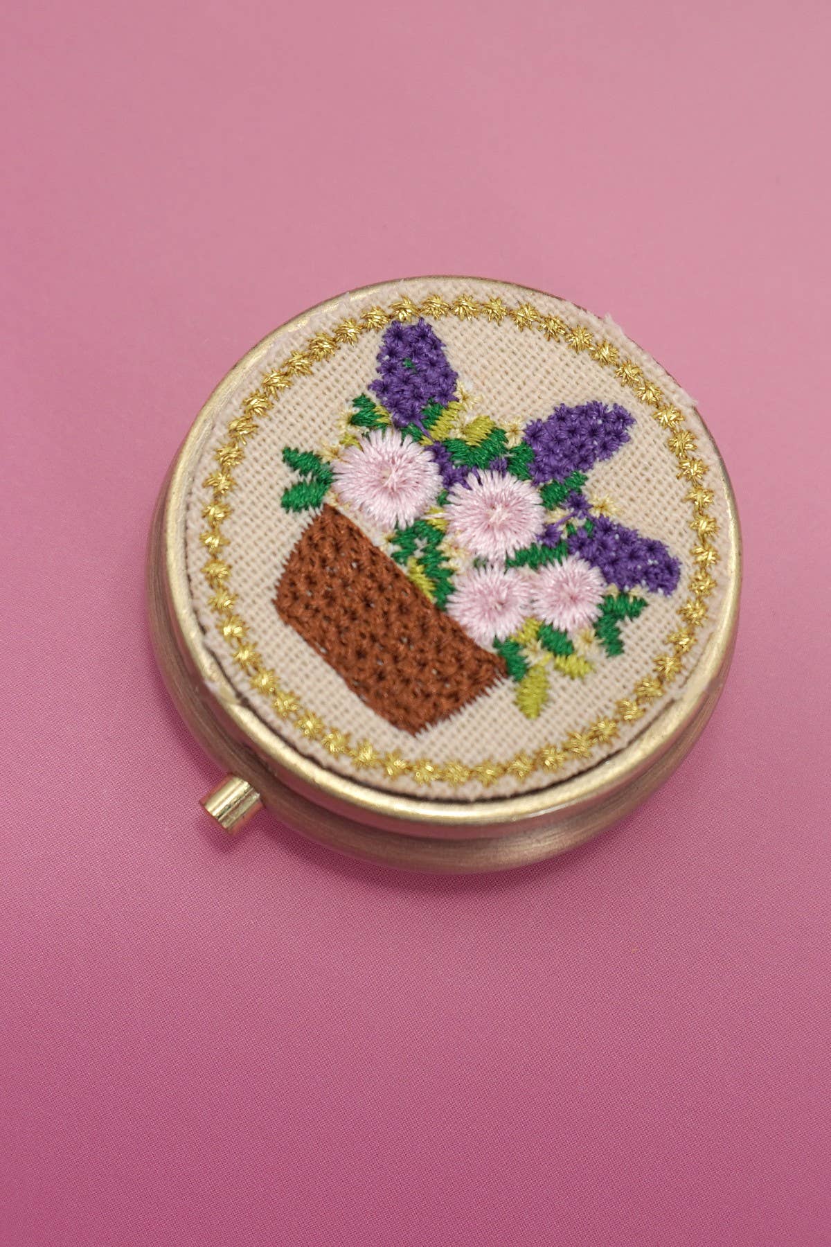 Round embroidered compact mirror with floral design on a pink background