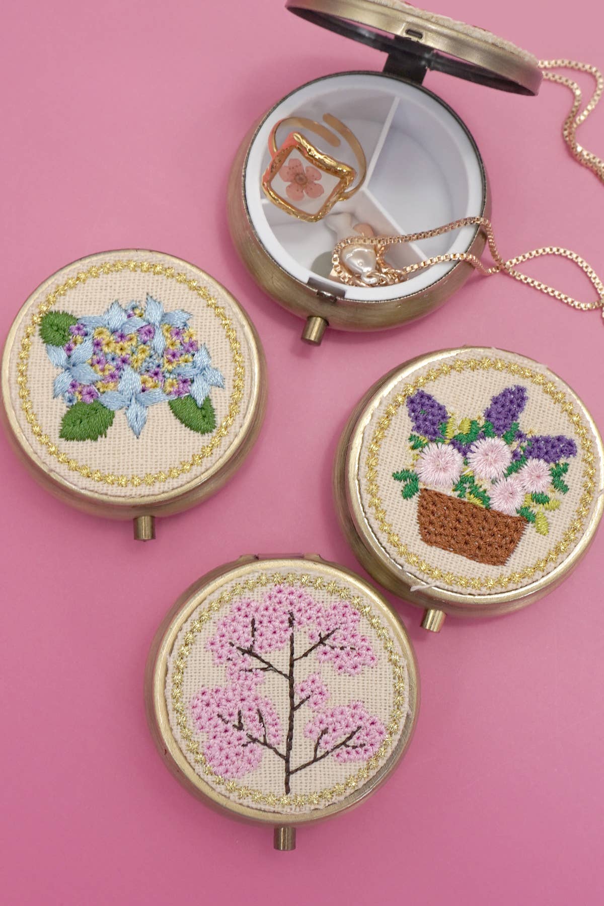 Three round embroidered cases with floral designs on a pink background