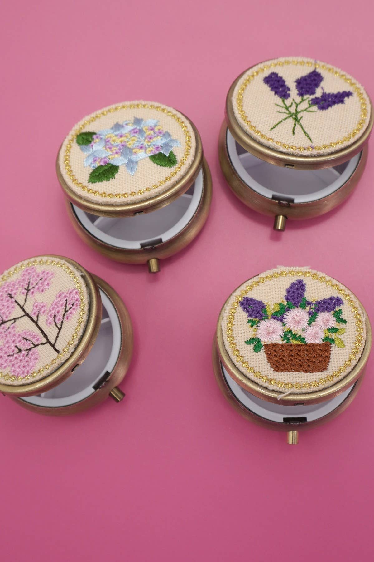 Four round embroidered boxes with floral designs on a pink background