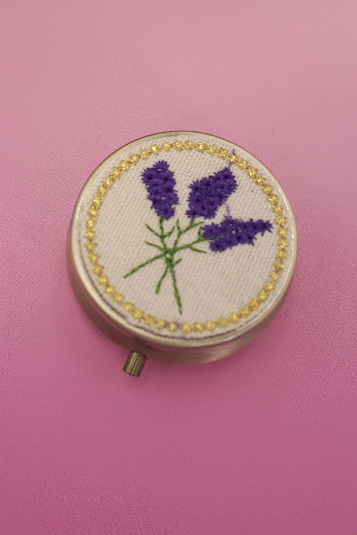 Round embroidered hoop with lavender design on a pink background