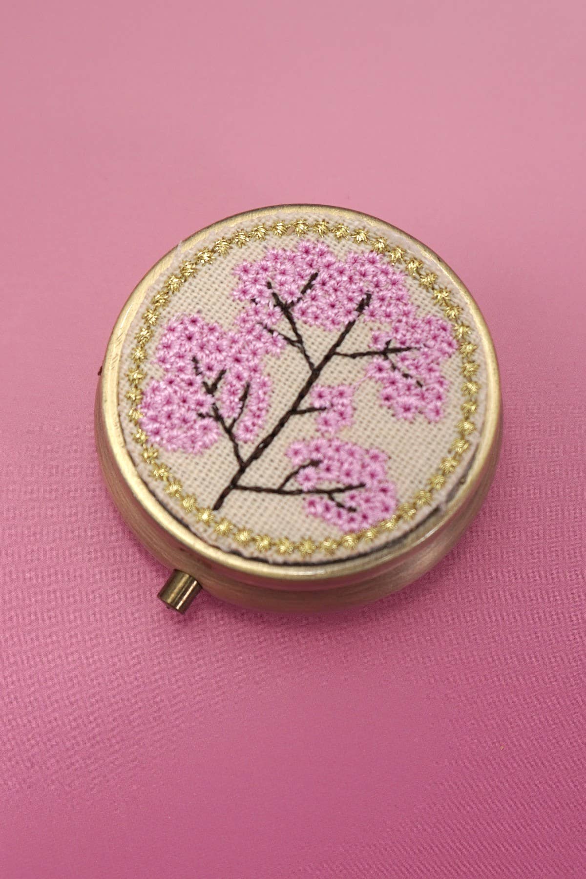 Round embroidered box with pink floral design on a pink background