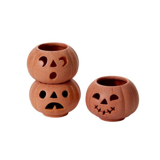 Three stackable grinning pumpkin votives with terracotta finish and reactive glaze, glowing softly with battery-operated tealights, styled on a cozy fall tabletop with autumn leaves.