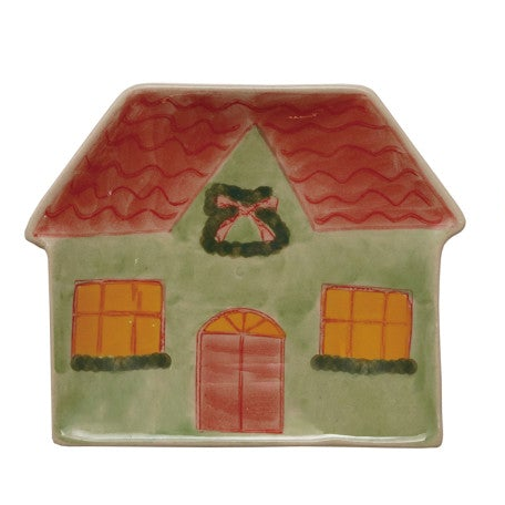 A ceramic Christmas house trinket dish with a light green body, a red wavy roof, a red door, orange-yellow windows, and a green wreath with a red bow on the front.
