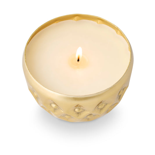 Illume Winter White candle burning in a warm gold pressed-metal vessel with textured geometric pattern and scalloped rim.