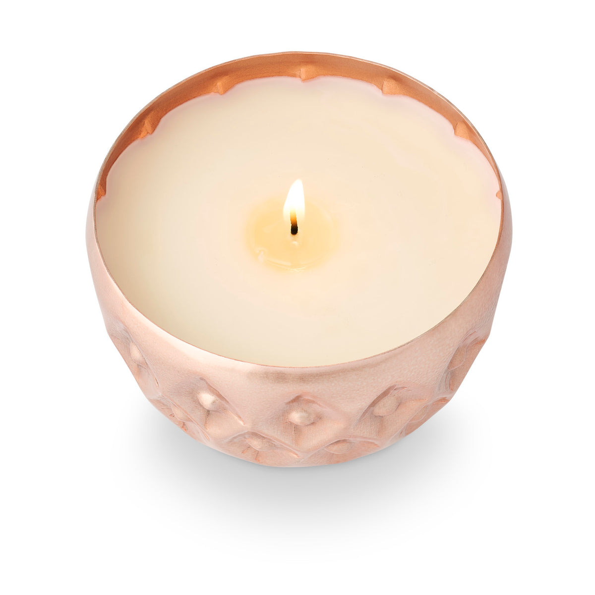 Illume Woodfire candle burning in a warm metallic pressed-metal vessel with dimensional pattern and scalloped rim.