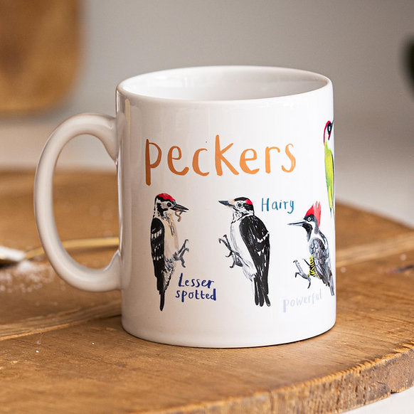 White mug with illustrations of woodpeckers and text on a wooden surface