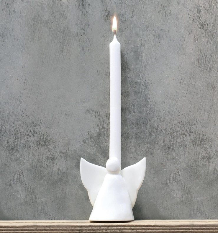 White ceramic angel candle holder with a lit candle on a gray concrete background
