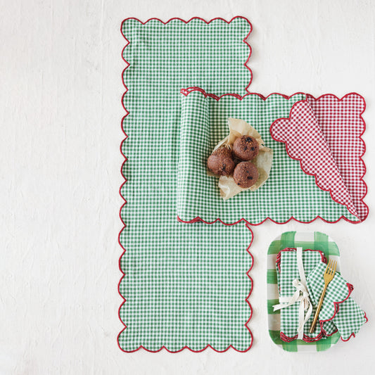 Reversible cotton scalloped table runner styled with green gingham and red striped sides for a festive holiday table.