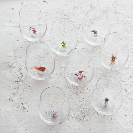 Clear glass tumblers with small decorative figures on a textured white surface