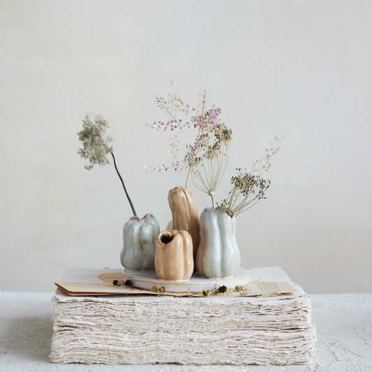 Decorative arrangement with vases and dried flowers on a stack of books against a plain background
