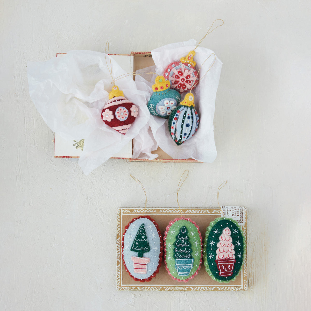 Three oval wool felt Christmas tree ornaments with embroidered trees in blue, red, and pink flowerpots, finished with beads and scalloped trim.